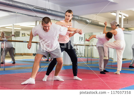 Girl performing elbow strike and wristlock to man in self defence training 117037358