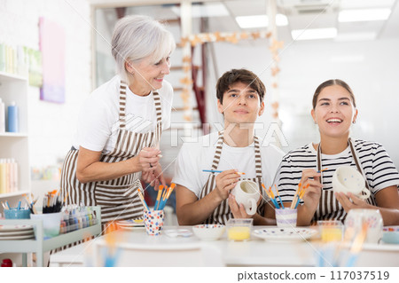 Group of cheerful people painting ceramic dishware in pottery class Group of cheerful people painting ceramic dishware in pottery class 117037519