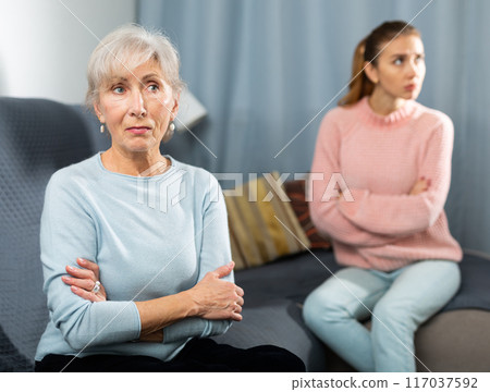 Offended elderly woman sitting on sofa after quarrel with daughter 117037592