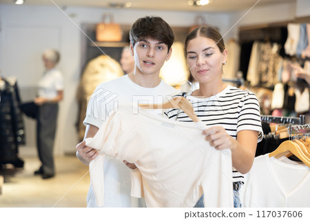 Young girl consults with male friend about purchasing sweater during shopping 117037606