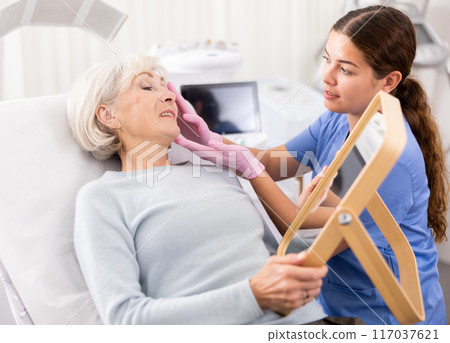 Old woman having consultation about face aesthetic while looking in the mirror 117037621