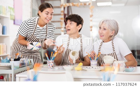 Group of cheerful people painting ceramic dishware in pottery class Group of cheerful people painting ceramic dishware in pottery class 117037624