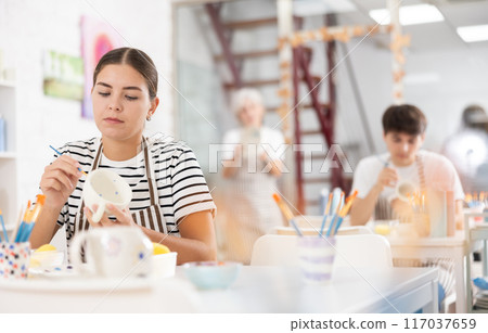 Young female artist painting ceramic cup in pottery workshop Young female artist painting ceramic cup in pottery workshop 117037659