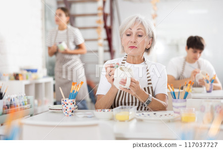Experienced female artist painting ceramic cup in pottery workshop Experienced female artist painting ceramic cup in pottery workshop 117037727