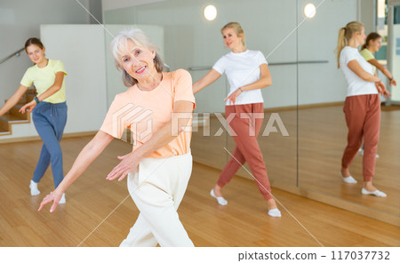 Positive woman doing aerobics exercises with group of people in dance center 117037732