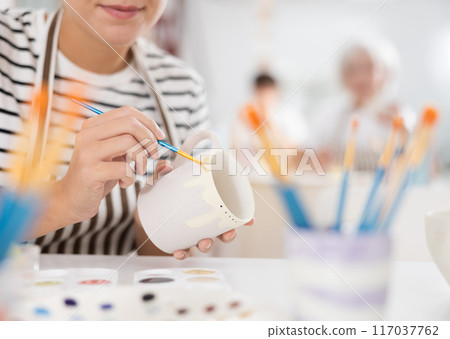 Hands of female artisan painting mug in pottery workshop 117037762