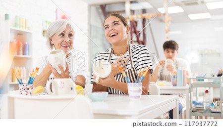 Cheerful elderly and young wowen painting mugs in pottery masterclass 117037772
