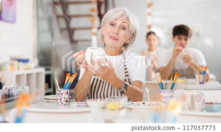Experienced female artist painting ceramic cup in pottery workshop Experienced female artist painting ceramic cup in pottery workshop 117037773