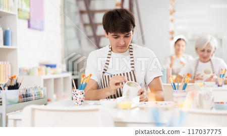 Talented young artisan applying design to ceramic mug in pottery studio 117037775