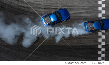 Aerial top view two cars drifting battle on asphalt race track with lots of smoke from burning tires, Two race cars competition drift battle view from above. Aerial top view two cars drifting battle on asphalt race track with lots of smoke from burning tires, Two race cars competition drift battle view from above. 117038745