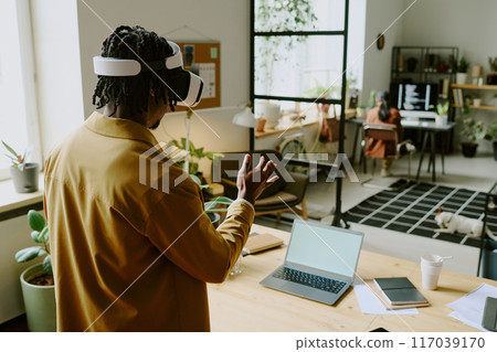 High angle view shot of young African American male programmer using VR headset at work in modern IT company office 117039170