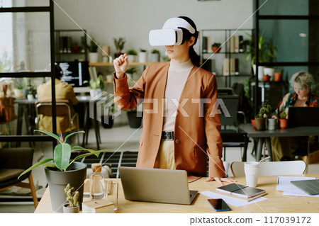 Young Asian female developer wearing headset using VR software at work in modern eco-friendly office of IT company 117039172