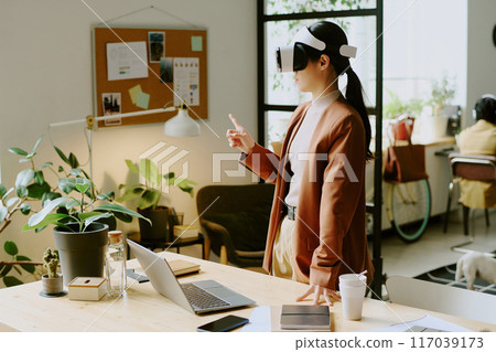 Young Asian female programmer wearing VR headset testing new app at work in modern IT company office, copy space 117039173