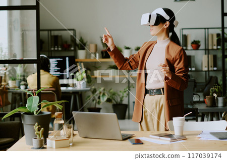 Young Asian female developer wearing VR headset testing virtual application at work in leading IT company office with biophilic design Young Asian female developer wearing VR headset testing virtual application at work in leading IT company office with biophilic design 117039174