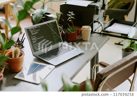 High angle view of digital tablet and laptop with code on screen on desk at workplace with biophilic design, copy space 117039258