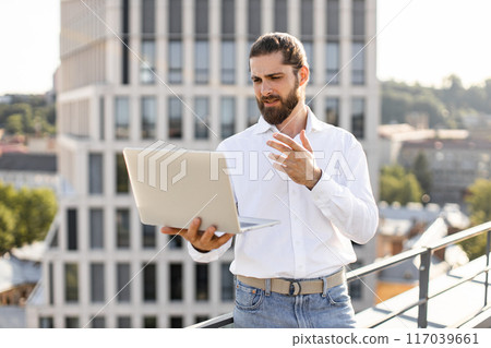 Businessman working on laptop outside modern office building 117039661