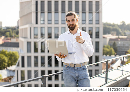 Confident business man giving thumbs up on rooftop with laptop Confident business man giving thumbs up on rooftop with laptop 117039664