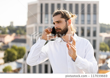 Businessman talking on phone outdoors in business district Businessman talking on phone outdoors in business district 117039669
