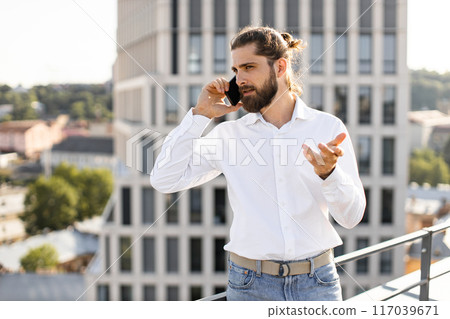 Businessman talking on phone on rooftop terrace with cityscape background Businessman talking on phone on rooftop terrace with cityscape background 117039671