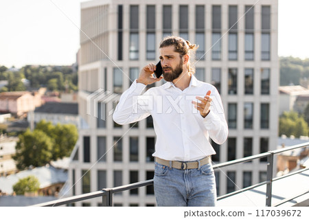 Businessman talking on cell phone on rooftop with city view Businessman talking on cell phone on rooftop with city view 117039672