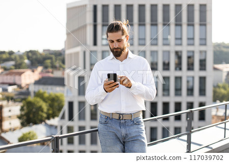 Business professional using smartphone on rooftop with city view 117039702