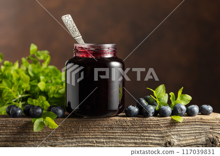 Jar of blueberry jam with fresh berries on an old wooden table. 117039831
