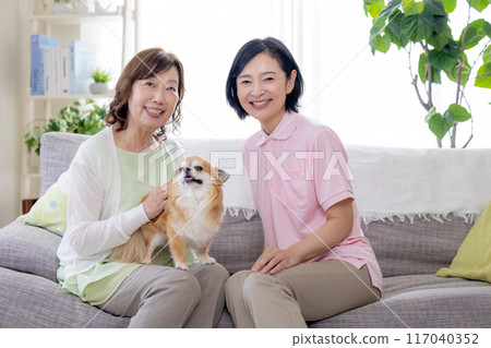 護理：高級婦女和護理人員在沙發上撫摸狗 117040352