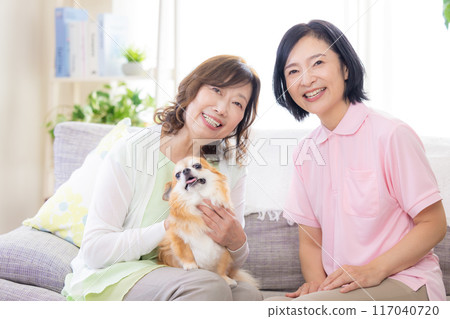Caregiving: Senior woman and caregiver petting a dog on the sofa Caregiving: Senior woman and caregiver petting a dog on the sofa 117040720