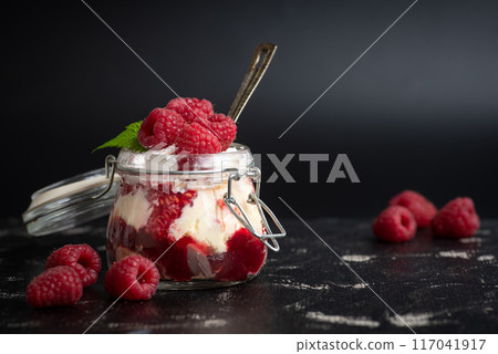 Mason jar filled with layered dessert, topped with fresh raspberries and mint. 117041917
