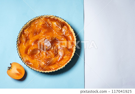 Delicious persimmon tart on pastel blue background showcasing appealing dessert 117041925