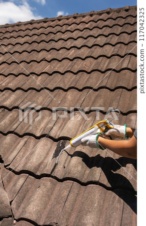 Worker man using silicone sealant adhesive to fix crack of the old tile roof. Worker man using silicone sealant adhesive to fix crack of the old tile roof. 117042325