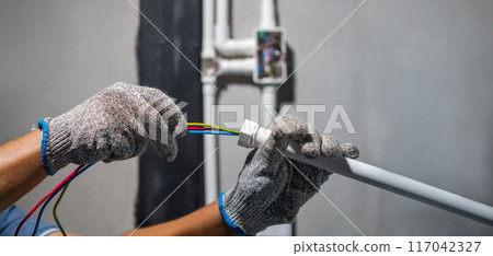 Electrician pulling wire through PVC Conduit from solar inverter system. Electrician pulling wire through PVC Conduit from solar inverter system. 117042327