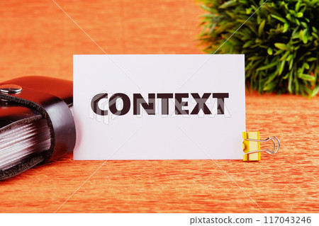Conceptual context symbol. Copy space. Context word written on a business card near a leather business card holder in a composition with a green plant in front of an orange background Conceptual context symbol. Copy space. Context word written on a business card near a leather business card holder in a composition with a green plant in front of an orange background 117043246