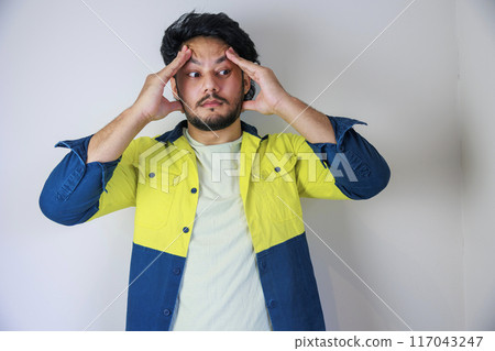 A man wearing work clothes holding his head A man wearing work clothes holding his head 117043247