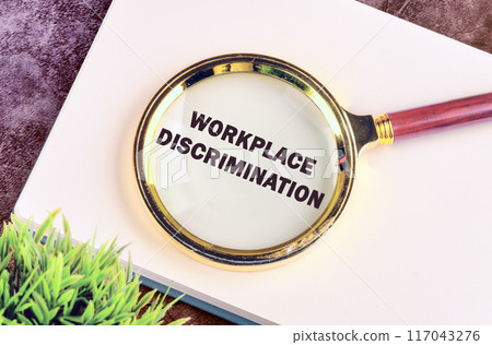 WORKPLACE DISCRIMINATION text through a magnifying glass in a business book, top view, conceptual photo 117043276