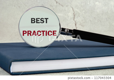 BEST PRACTICES text written through a magnifying glass located on a business notebook against a wall background 117043304
