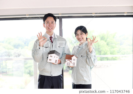 Male and female workers hold a model of a house and make an OK pose 117043746