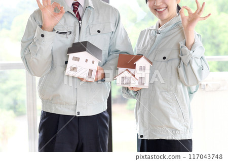 Male and female workers hold a model of a house and make an OK pose Male and female workers hold a model of a house and make an OK pose 117043748