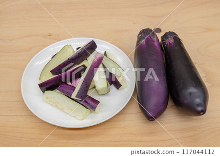Two eggplants and one cut eggplant served on a plate Two eggplants and one cut eggplant served on a plate 117044112