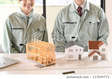 Asian man and woman in work clothes in front of a model house 117044773