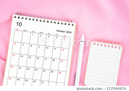 October 2024 month calendar and pen with open diary on pink fabric background. 117044974