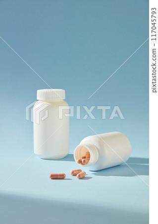 Advertising mockup for medicine products with two unbranded bottle featured side by side on blue background. Some purple drugs fall to the table from the bottle, space for text 117045793