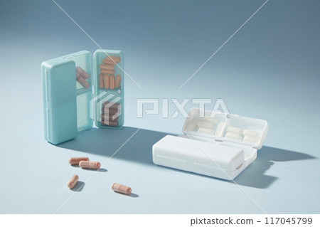 Two pill boxes contains purple and white pills featured on blue background. Template photo to design advertising pic from high angle shot with empty space for adding elements of designing Two pill boxes contains purple and white pills featured on blue background. Template photo to design advertising pic from high angle shot with empty space for adding elements of designing 117045799