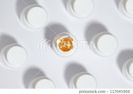 Minimalist photography from above with a series of white medicine jars, which arranged evenly on a white surface. In the middle, standing out with yellow color pills in an opened drug jar, copy space 117045808