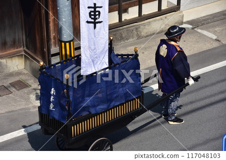 日本岐阜縣高山市，春季高山節，一名穿著法衣和金卡薩的男子，推著一輛掛著旗幟的手推車 117048103