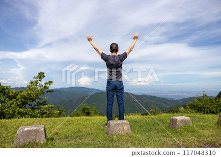 Back view of a senior man climbing Mt. Ibuki and spreading his arms to feel a sense of freedom 117048310