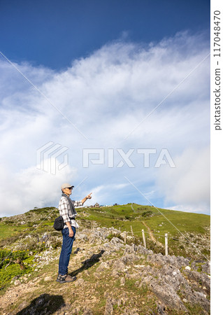 一位戴著帽子和毛巾的老人爬上伊吹山,用手指指著風景 一位戴著帽子和毛巾的老人爬上伊吹山,用手指指著風景 117048470