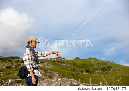 一位戴著帽子和毛巾的老人爬上伊吹山,用手指指著風景 一位戴著帽子和毛巾的老人爬上伊吹山,用手指指著風景 117048475