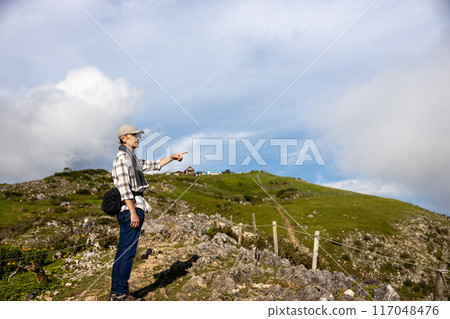 A senior man wearing a hat and a towel on his head who has climbed Mt. Ibuki and is pointing at the view A senior man wearing a hat and a towel on his head who has climbed Mt. Ibuki and is pointing at the view 117048476