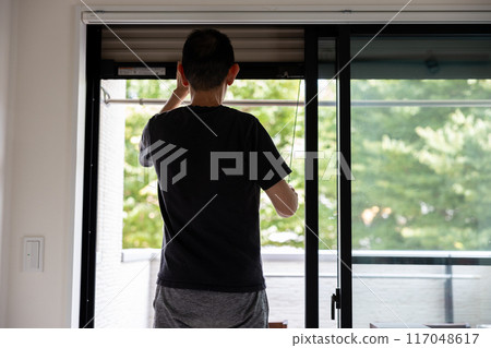 一名男子打開房間窗帶的後視圖 117048617